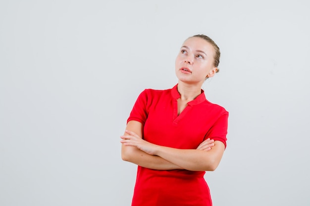 Young woman looking up with crossed arms in red t-shirt and looking pensive