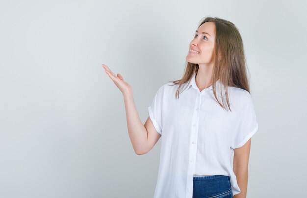 Young woman looking up with hand sign in white t-shirt, jeans and looking cheerful