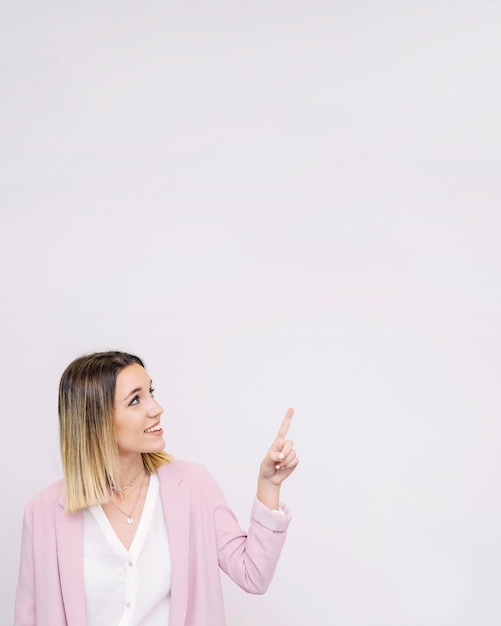 Free photo young woman looking at white empty backdrop pointing upward