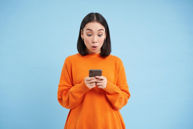 Young woman looks amazed at her cellphone reads exciting news found good deal online on mobile appli