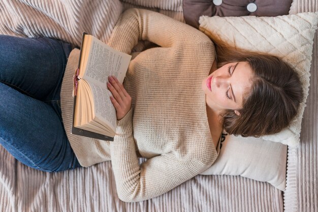 Молодая женщина лежит на кровати и читает книгу