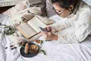 Free photo young woman lying on bedsheet with mobile phone