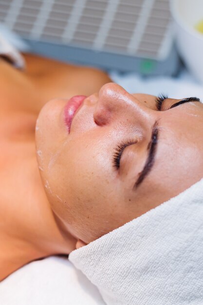 Young woman lying on cosmetologist's table during rejuvenation procedure.