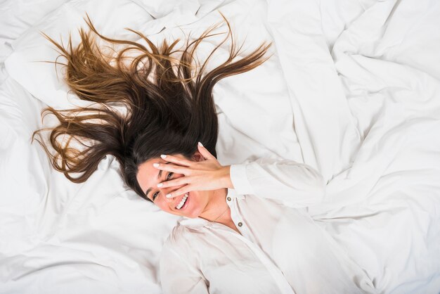 Young woman lying on crumpled bed peeking through finger