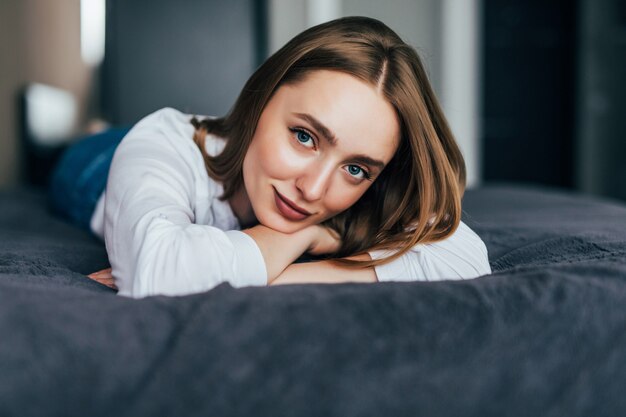 Young woman lying down with a quilt over her as she looks forward and a hand upon her cheek