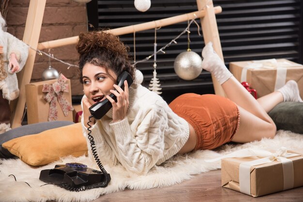 Young woman lying on fluffy carpet speaking on telephone