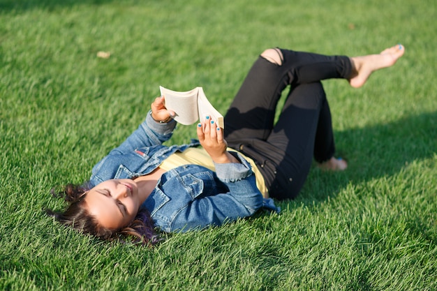 여름에 공원에서 녹색 잔디밭에 누워 책을 읽는 젊은 여자