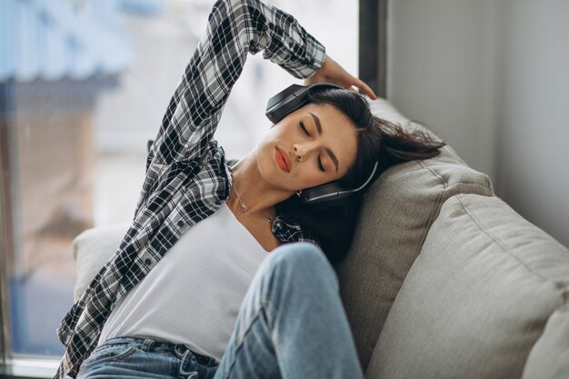 Young woman lying on the sofa in earphones listening to music