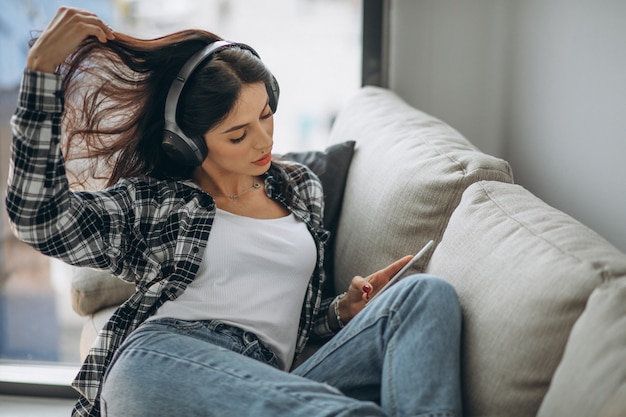 Young woman lying on the sofa in earphones listening to music