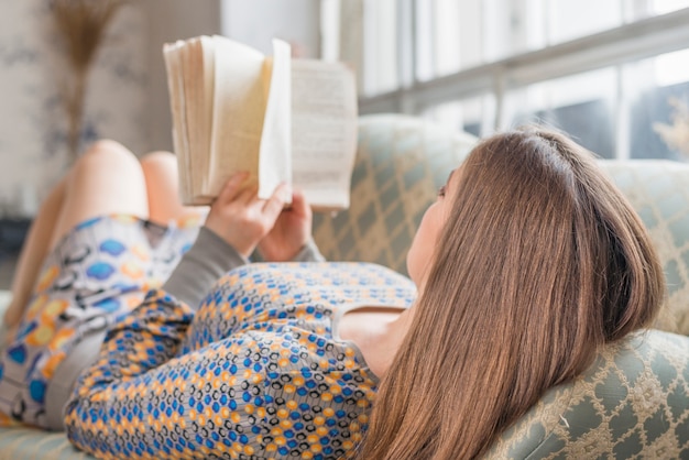 Молодая женщина лежит на диване и читает книгу