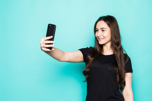 Young woman make take selfies isolated on turquoise wall