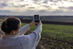 Free photo young woman makes a photo of the field by smartphone