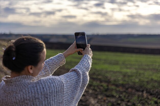 若い女性がスマートフォンで野原の写真を撮る