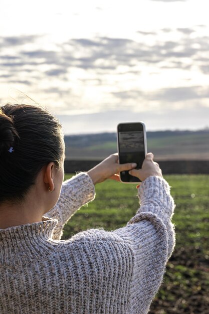 Young woman makes a photo of the field by smartphone