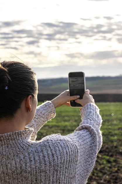 若い女性がスマートフォンで野原の写真を撮る