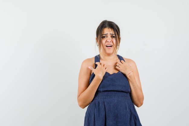 Young woman making asking 'me?' gesture in dress and looking sad