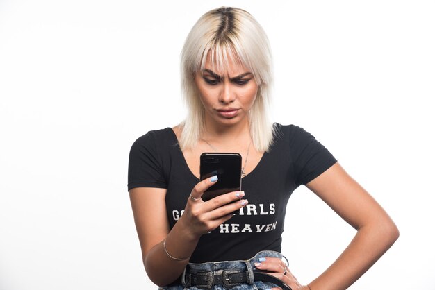 Young woman making call with serious expression on white wall.