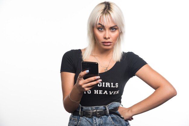 Young woman making call with serious expression on white wall.