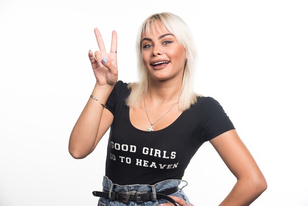 Young woman making hand sign on white wall.