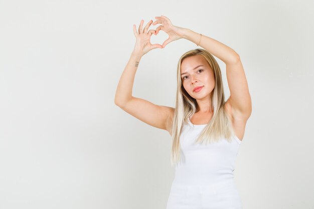 Young woman making heart shape over head in singlet 