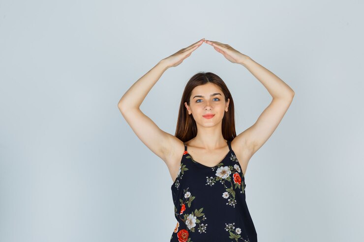 ブラウスで頭上に家の屋根のジェスチャーをし、自信を持って見える若い女性。正面図。