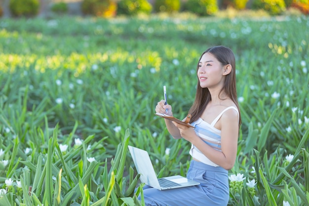 花畑に座ってメモ帳でメモをとる若い女性