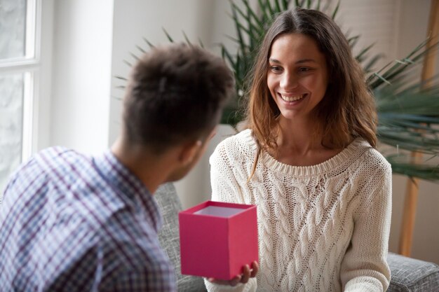 Young woman making present giving open gift box to husband