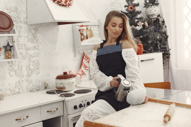 Young woman making shaped cookies for Christmas. Living room decorated with Christmas decorations in the background. Woman in a apron.