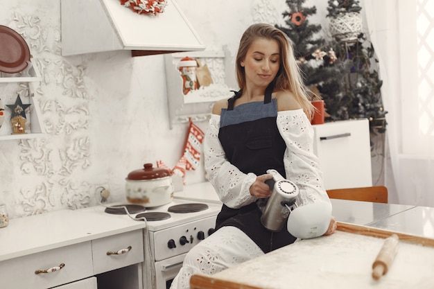 Молодая женщина, делая печенье на Рождество. Гостиная украшена рождественскими украшениями на заднем плане. Женщина в фартуке.