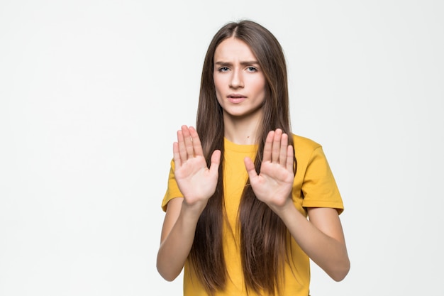 白い壁に分離された彼女の手で停止ジェスチャーを作る若い女性