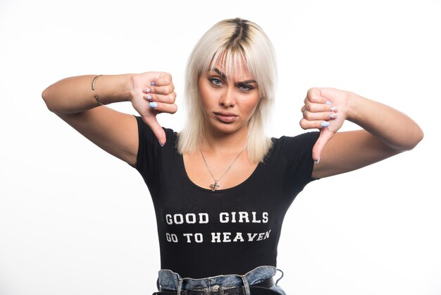 Young woman making thumbs down sign on white wall.