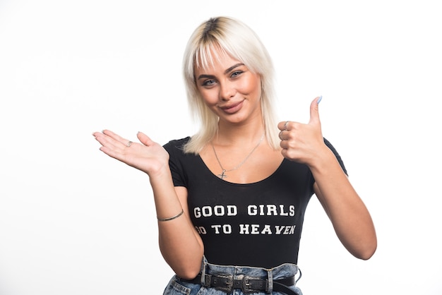 Young woman making thumbs up signs on white wall.