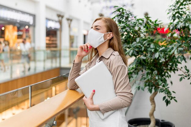 Young woman at mall with laptop wearing mask