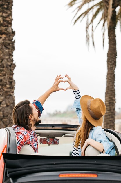 Young woman and man showing symbol of heart and leaning out from car