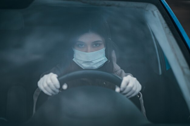 Young woman in a mask and gloves driving a car.