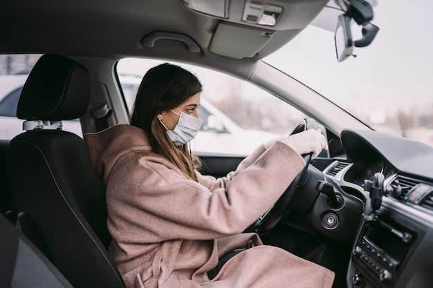 マスクと手袋をはめて車を運転する若い女性。