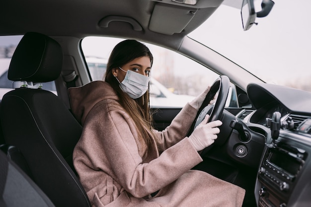 Free photo young woman in a mask and gloves driving a car.