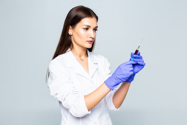 Young woman medic with a syringe in her hand on white wall.