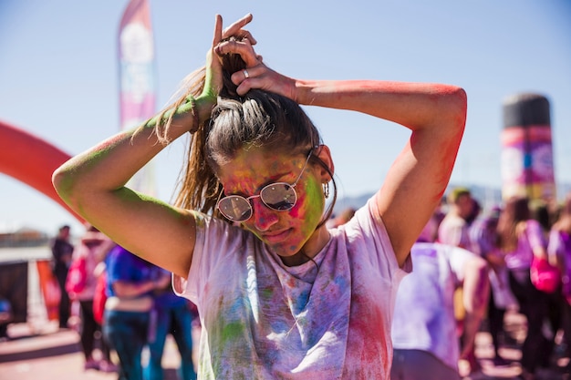 무료 사진 야외에서 그녀의 머리를 묶는 선글라스를 착용하는 holi 색상의 젊은 여성 엉망