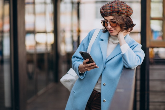 Young woman model in blue coat by the cafe,using phone