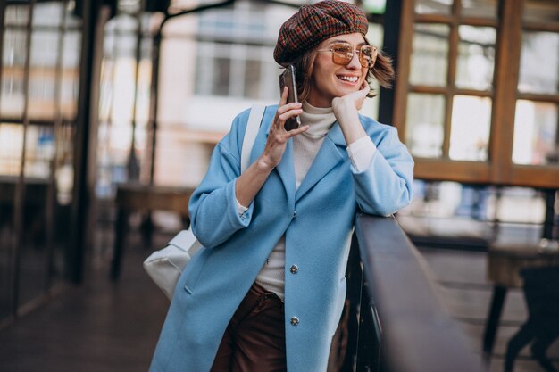 電話を使用して、カフェで青いコートの若い女性モデル