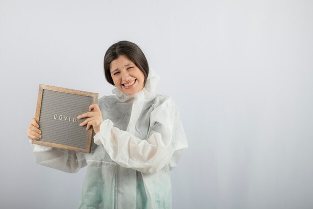 модель молодой женщины в защитном лабораторном халате, стоящем на белой стене.