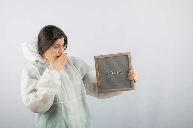 young woman model in defensive lab coat standing on white wall. 