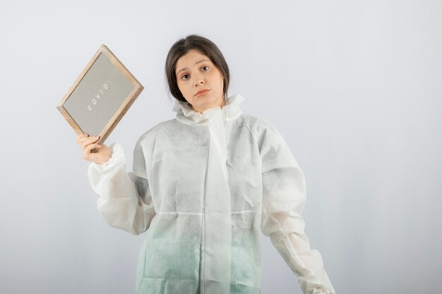 young woman model in defensive lab coat standing on white wall. 