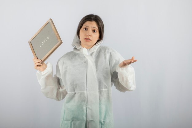 young woman model in defensive lab coat standing on white wall. 