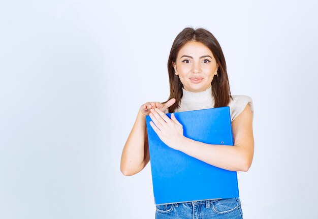 young woman model holding a blue folder over white wall.