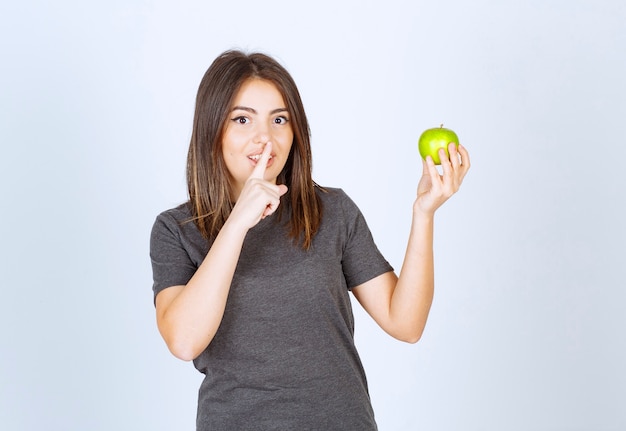 young woman model holding a green apple and doing silent sign .