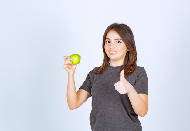 young woman model holding a green apple and showing a thumb up.