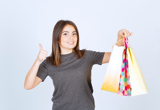 Foto gratuita un modello di giovane donna che tiene in mano molte borse della spesa e mostra un pollice in su.