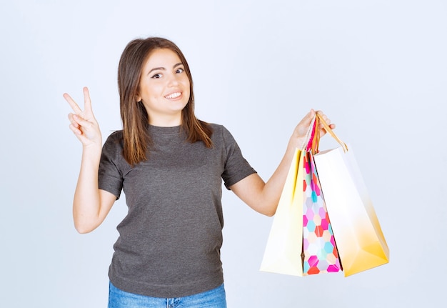 A young woman model holding a lot of shopping bags and showing victory sign.